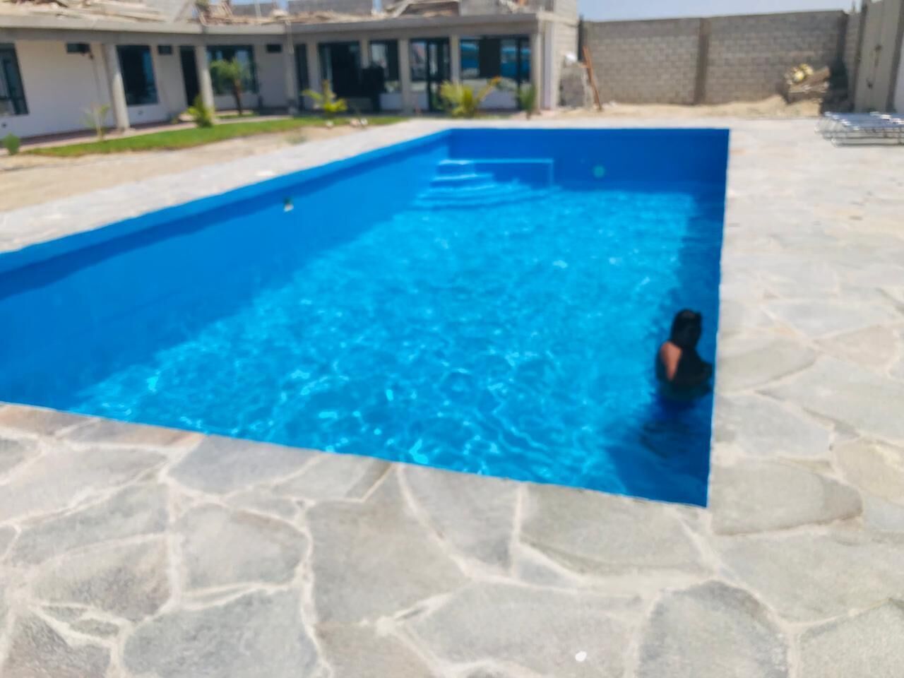 Una piscina con agua azul cristalina, rodeada de baldosas de piedra.