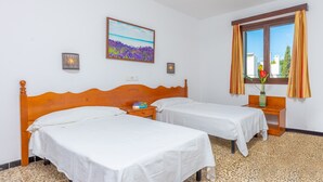 Ein Hotelzimmer mit zwei Einzelbetten, einem Holzkopfstück, einem kleinen Nachttisch mit einem Buch, einem Wandbild und einem Fenster mit Vorhängen.