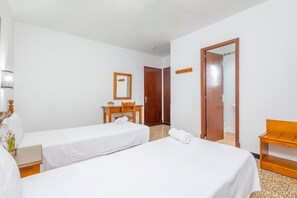 Ein Hotelzimmer mit zwei Einzelbetten, einem Holztisch, einem Stuhl, einem kleinen Tisch mit Blumenvase und einem Spiegel an der Wand.