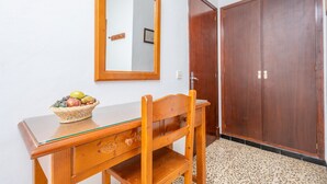 Un escritorio de madera con cubierta de vidrio, una cesta de mimbre para frutas, una silla de madera, un espejo y dos puertas de madera.