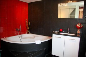 Une salle de bain moderne avec une grande baignoire, un meuble-lavabo avec un miroir et un mur d’accent rouge.