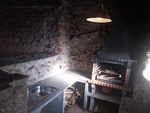 Une cuisine rustique en pierre, dotée d’un four encastré, d’un évier et d’un luminaire suspendu.