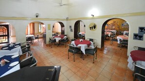 A dining area with tables and chairs, a ceiling fan, and a mural on the wall. - Shama Tourist Resort (Gurugram)