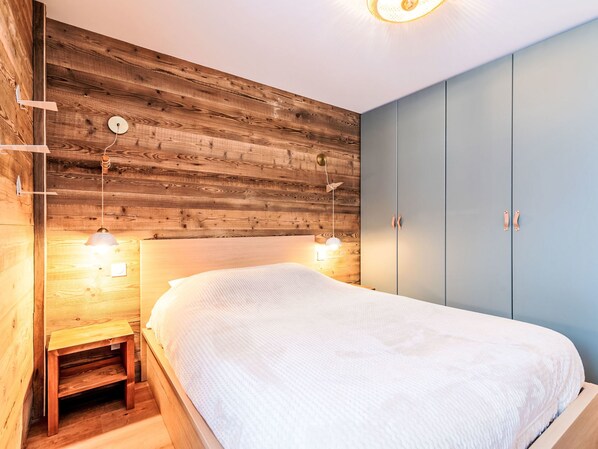Une chambre à coucher avec une tête de lit en bois, un lit avec une literie blanche, deux lampes de chevet et une armoire bleue.