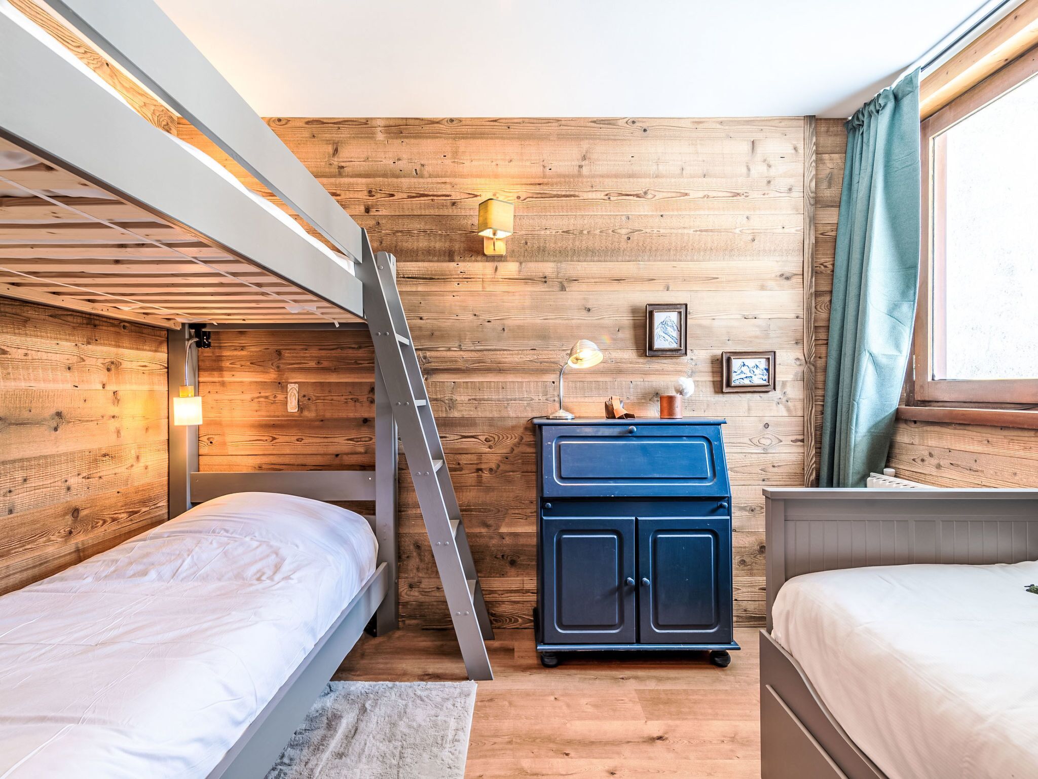 A compact room with bunk beds, a small desk with a lamp, and a window with curtains.