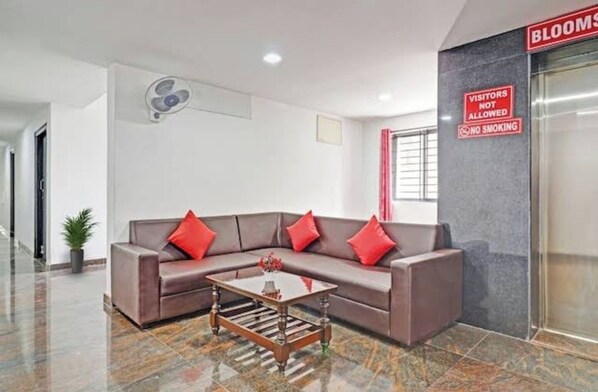 A modern waiting area with a brown sofa, red cushions, and a coffee table. A sign on the wall indicates visitors are not allowed and no smoking is permitted. - The Blooms Stay Inn (Bangalore)