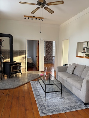 A living room with a sofa, a glass coffee table, a fireplace, a ceiling fan, and a view through an open door. - Mercantile House Guest Suite near Roblin Lake (hidden gem in PEC) ST-2023-0061 (Prince Edward)