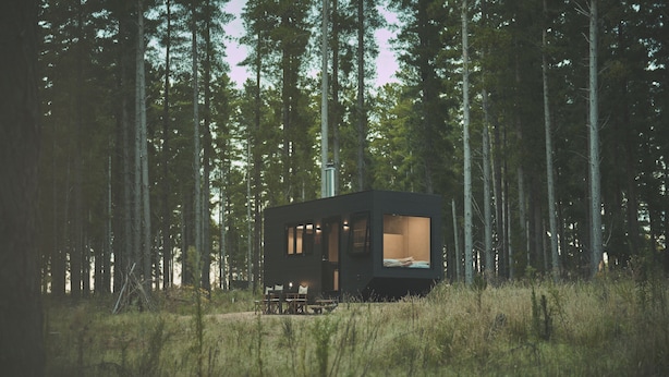 A small cabin in a forest with a clear view of the interior through the windows.