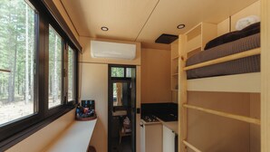 A compact room with bunk beds, a kitchenette, a sink, and a window overlooking a forest.