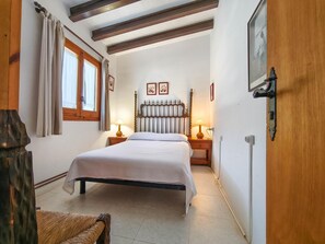 Ein Schlafzimmer mit einem Bett, zwei Nachttischen inklusive Lampen, einem Holz-Kopfteil, einem Fenster mit Vorhängen und einer Tür mit einem Bild.