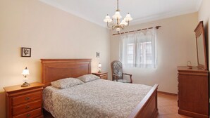 Une chambre à coucher comprenant un lit, une table de chevet, une chaise, une commode et un lustre.