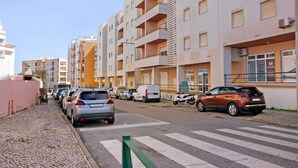 Une rue bordée d’immeubles résidentiels à plusieurs étages, de voitures garées et d’un passage piéton.