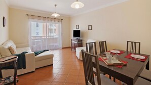 Un salon avec un canapé, une télévision, une table à manger agrémentée de sets de table rouges et un balcon avec vue.