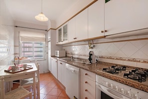 A kitchen with white cabinets, a gas stove, a dishwasher, and a window with a view. - Mar Salgado Beach Apartment with Shared Pool, Shared Garden and Wi-Fi (Armação de Pêra)