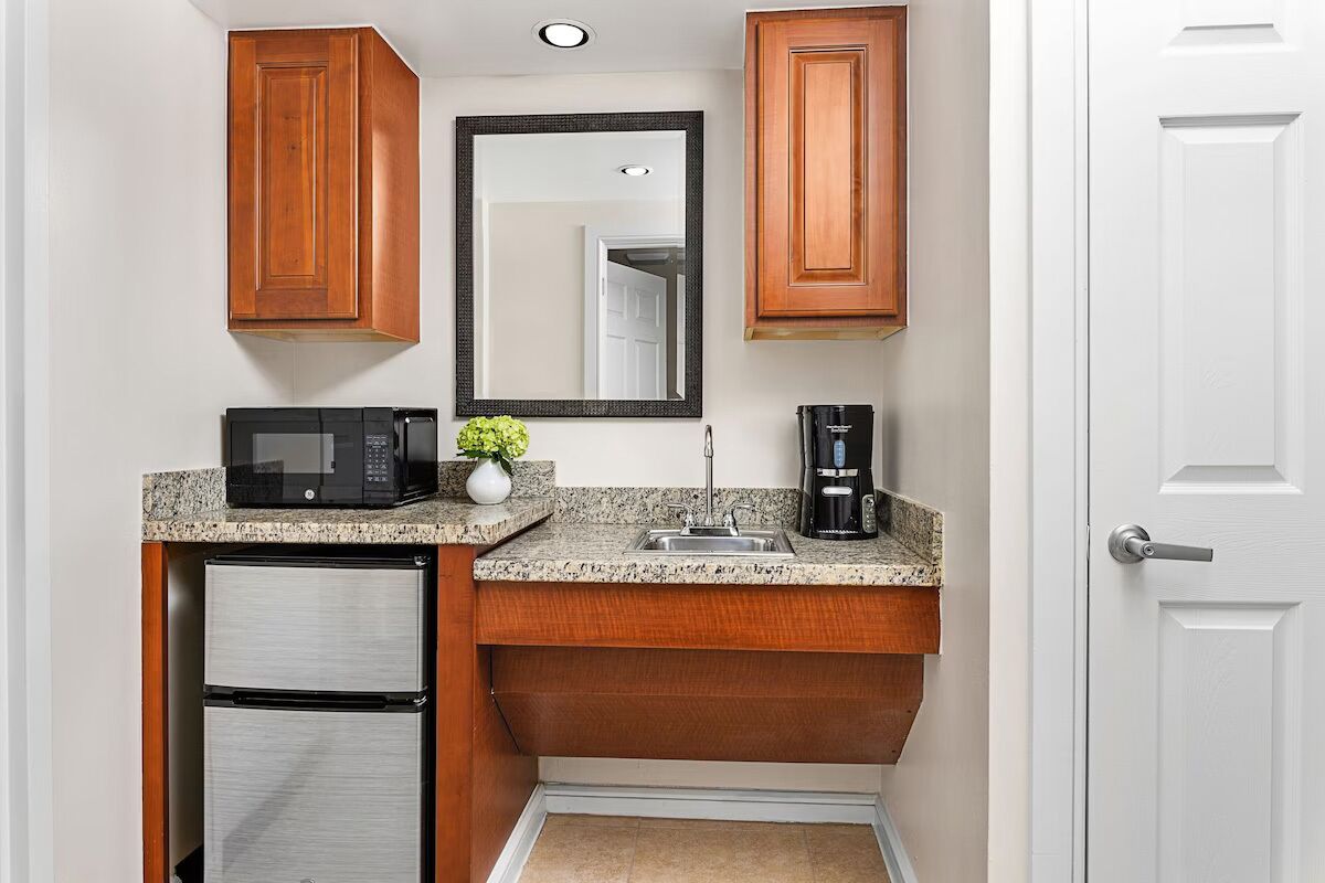 A compact kitchenette with wooden cabinets, a microwave, a coffee maker, and a small refrigerator.