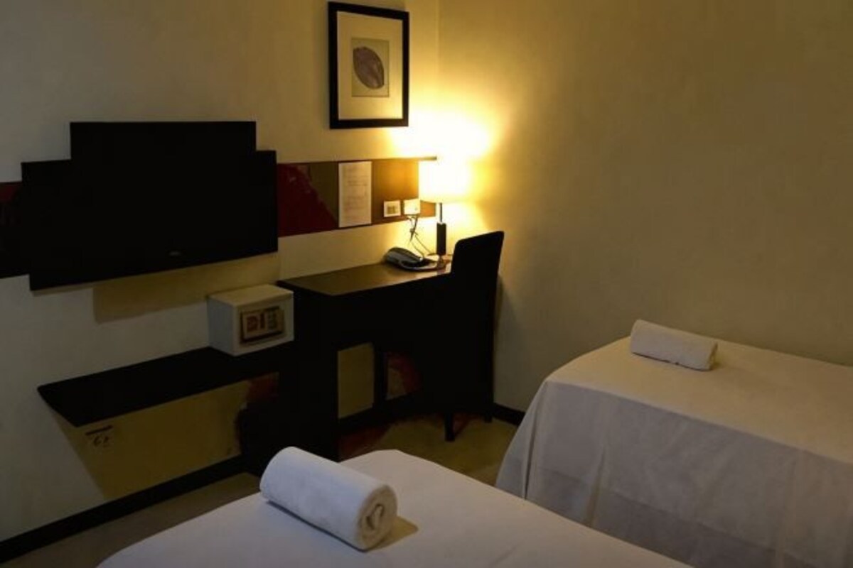A hotel room with two beds, a desk, a television, and a lamp.