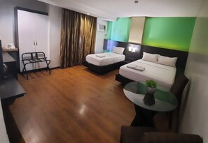 Habitación de hotel con dos camas, un escritorio, una silla, una mesita con una planta y una cortina.