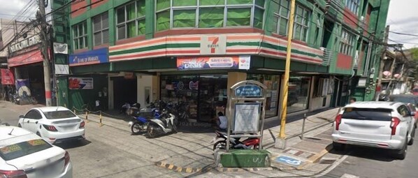 Una tienda 7-Eleven con fachada verde, coches y motocicletas estacionados afuera.