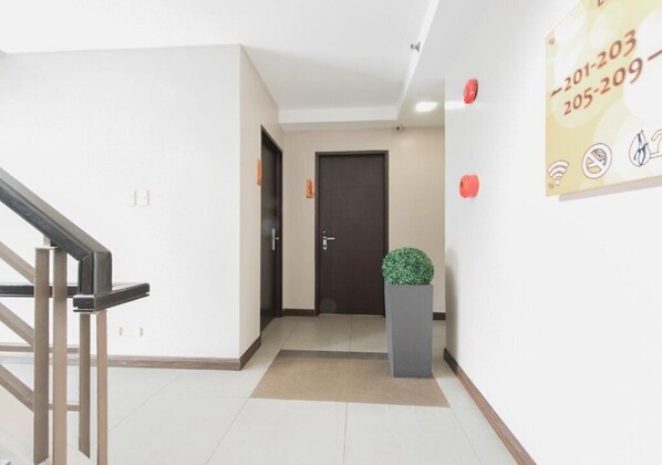 A hotel corridor with a dark door, a small potted plant, and a wall-mounted sign with contact numbers. - Lorenzzo Suites Hotel (Makati)