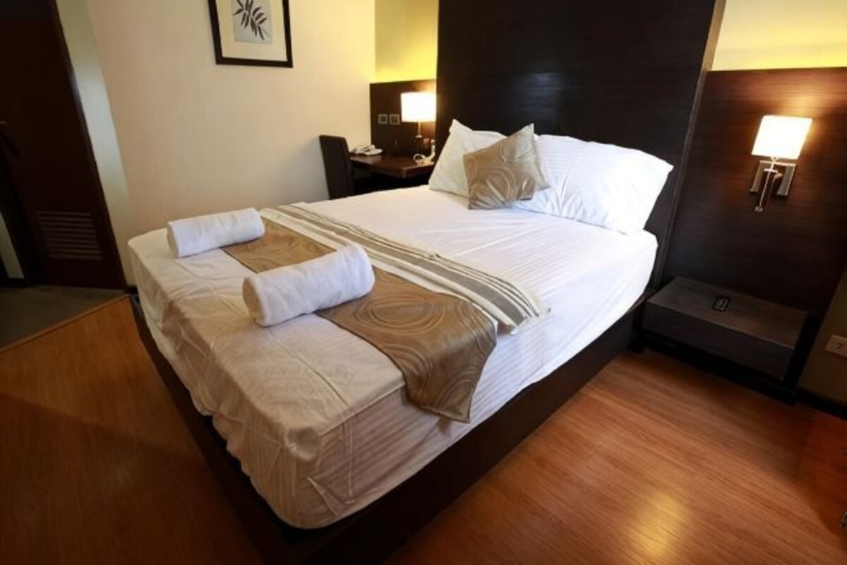 A hotel room with a large bed, bedside tables, a desk, and a lamp.