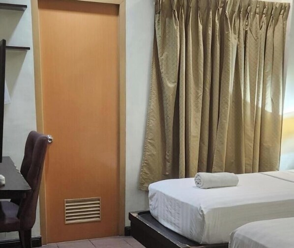 Una habitación de hotel con puerta de madera, una cama con ropa blanca y cortinas color beige.