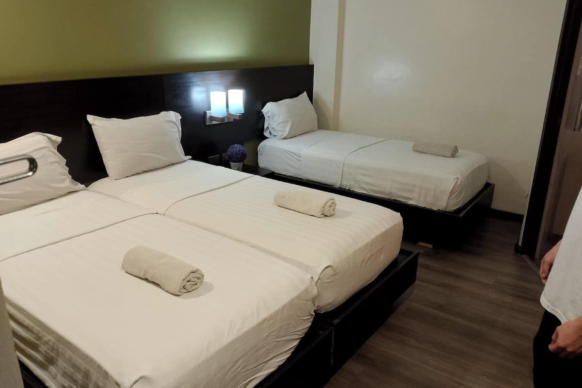 Ein Hotelzimmer mit zwei Betten, jeweils mit weißer Bettwäsche und Kissen, einer Kopfteilbeleuchtung an der Wand und einem Holzboden.
