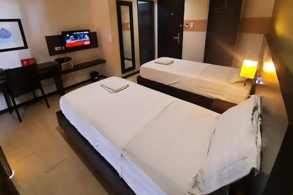 Ein Hotelzimmer mit zwei Einzelbetten, einem Schreibtisch mit Fernseher und einem Spiegel.