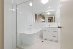 A modern bathroom with a glass-enclosed shower, a freestanding bathtub, and a white vanity with drawers.