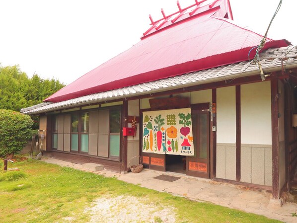 En traditionell japansk byggnad med ett rött tak, träfasad och en färgstark, hängande dekoration med motiv av grönsaker.