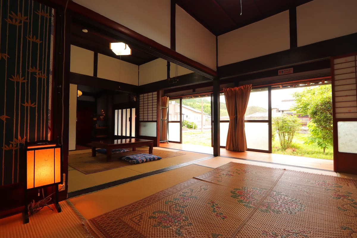 A traditional Japanese room with tatami flooring, a shoji screen, and a view of greenery outside.
