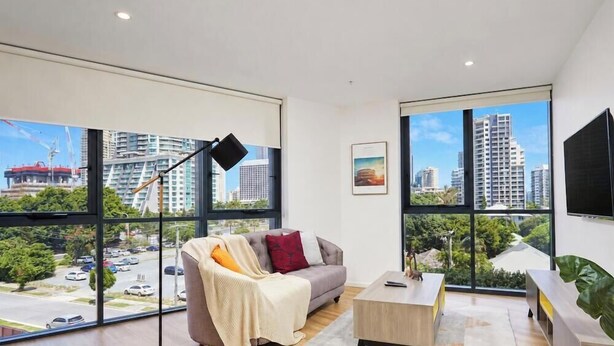A modern room with large windows, a sofa, a coffee table, and a TV. - Modern 1-Bedroom Apartment in Central Gold Coast (Surfers Paradise)