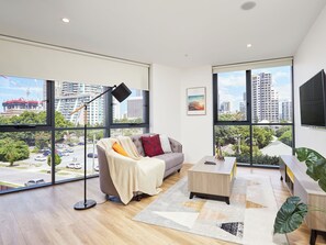 A modern living room with a sofa, coffee table, and large windows offering city views. - Modern 1-Bedroom Apartment in Central Gold Coast (Surfers Paradise)