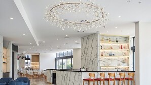 A modern hotel lobby with a marble reception desk, bar area with wooden chairs, and a unique chandelier. - Modern 1-Bedroom Apartment in Central Gold Coast (Surfers Paradise)