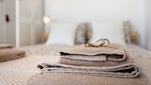 A neatly arranged stack of folded towels on a bed with a textured bedspread. - Apartment 'Torralta' with Sea View, Wi-Fi and Air Conditioning (Alvor)