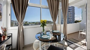 A balcony with a dining table set for two, a vase with yellow flowers, and a view of a tall building. - Apartment 'Torralta' with Sea View, Wi-Fi and Air Conditioning (Alvor)