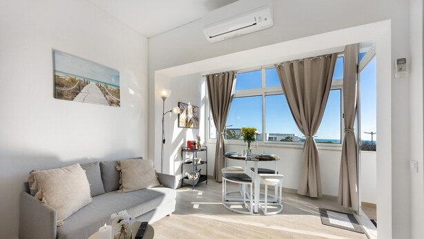 A modern living room with a sofa, a small table, a balcony with a view, and an air conditioning unit. - Apartment 'Torralta' with Sea View, Wi-Fi and Air Conditioning (Alvor)