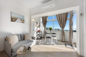 A modern living room with a sofa, a small table, a balcony with a view, and an air conditioning unit. - Apartment 'Torralta' with Sea View, Wi-Fi and Air Conditioning (Alvor)