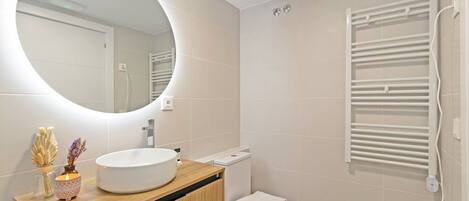 A modern bathroom with a round mirror, a wooden vanity, a white sink, and a towel rack.