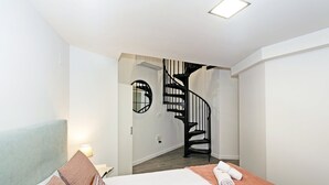 A hotel room with a bed, a desk, a chair, a round mirror, and a spiral staircase. - GuestReady - Flat near the Marina of Valencia (Valencia)