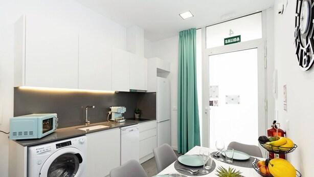 A compact kitchen with a washing machine, microwave, and coffee maker. A dining area with a table set for two, a fruit basket, and a potted plant. - GuestReady Essential - Flat near Valencia Marina (Valencia)