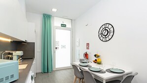 A modern kitchen with a coffee machine, a dining area with a white table set for four, and a wall clock. - GuestReady Essential - Flat near Valencia Marina (Valencia)