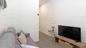 A modern living room with a grey sofa, a flat-screen TV on a wooden stand, and a small side table with a vase. - GuestReady Essential - Flat near Valencia Marina (Valencia)