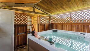 A man relaxing in a hot tub under a wooden ceiling with a wooden fence and a sign that reads "HOT TUBS".