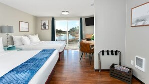 A hotel room with two beds, a desk, a chair, a TV, and a balcony with a view.