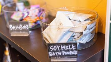 A glass container labeled "SOY MILK BATH POWDER" on a counter with a sign "Bath & Body" in the background.