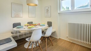 Een moderne eethoek met een ronde tafel, witte stoelen en een hangende lamp.