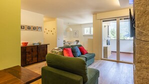 Een gezellige woonkamer met een groene bank, een houten salontafel en een eethoek met een tafel en stoelen.