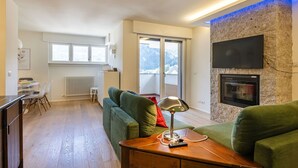 Een moderne woonkamer met een groene bank, een houten salontafel en een televisie die aan een stenen muur is bevestigd.