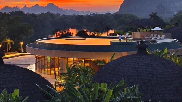 A resort with a pool, lounge chairs, and a mountain backdrop during sunset. - Chongzuo Wild Stay Collection - Wanxiang (Chongzuo)