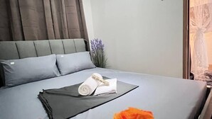 A bedroom with a bed, pillows, a bedside table, a vase with flowers, and a window with curtains. - 10th floor (Pasay)